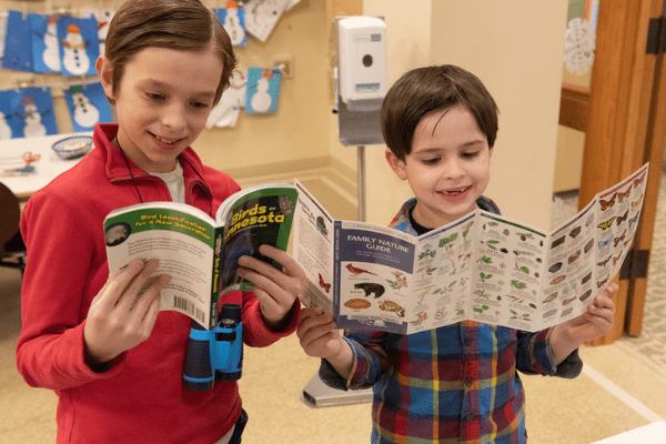 Two boys looking at book and guide from nature backpacks